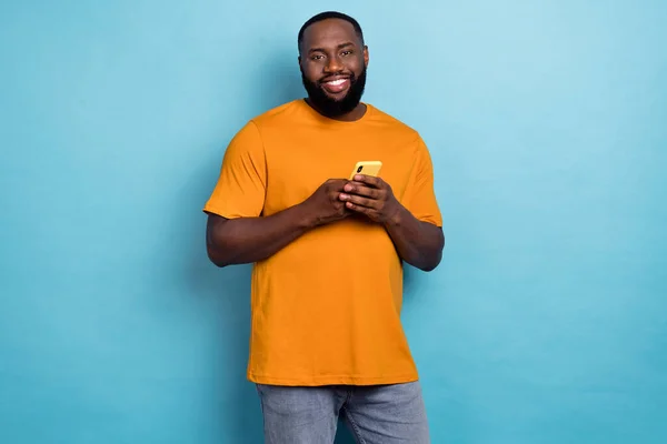 Photo of cheerful sweet guy dressed orange t-shirt communicating modern gadget isolated blue color background — ストック写真