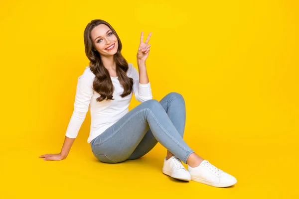 自信を持って素敵なフレンドリーな女性の写真が床に座るショーvサインは白いシャツを着用孤立黄色の背景 — ストック写真