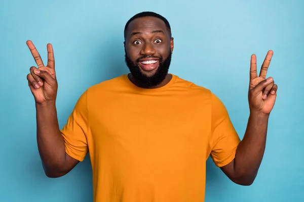Photo of excited funky guy dressed orange t-shirt showing two v-signs smiling isolated blue color background — стоковое фото