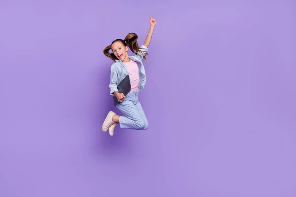Foto de muito animado menina da escola usar camisa jeans jumping segurando moderno dispositivo vazio espaço isolado cor roxa fundo — Fotografia de Stock