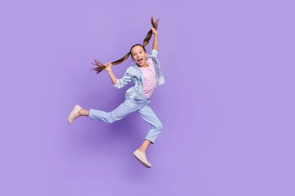 Photo of pretty funky little school girl wear denim shirt jumping high holding tails empty space isolated purple color background — ストック写真