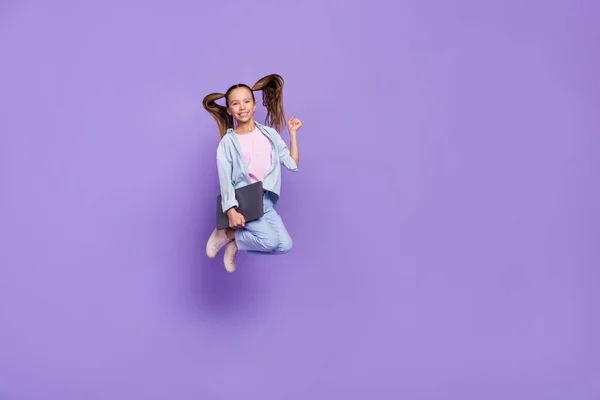 Foto de muito sorte pequena estudante vestida jeans camisa saltando segurando moderno gadget vazio espaço isolado cor violeta fundo — Fotografia de Stock