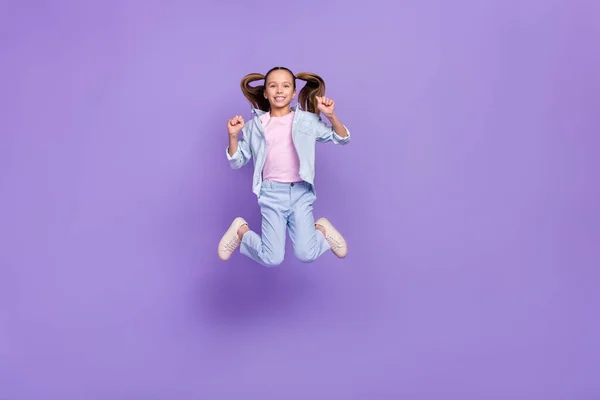 Foto de dulce suerte pequeña colegiala vestida jeans camisa saltando puños altos aislados color violeta fondo —  Fotos de Stock