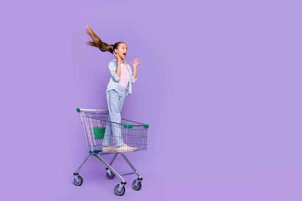 Fotó izgatott kis iskolás lány visel farmer ing bevásárló tálca vezető üres tér elszigetelt lila szín háttér — Stock Fotó