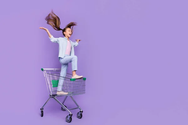 Фото блискучої збудженої маленької школярки в джинсовій сорочці водій магазину в лотку порожній простір ізольований фіолетовий кольоровий фон — стокове фото