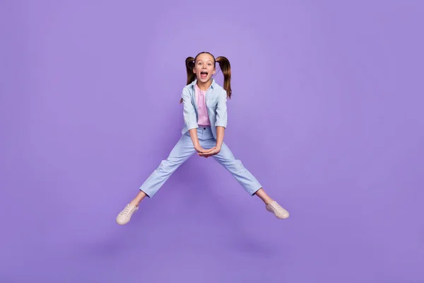 照片上漂亮的小女孩穿着牛仔裤衬衫跳过紫色的高背景 — 图库照片