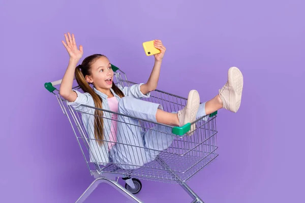 Foto di funky lucido poco scuola ragazza indossare denim camicia vassoio di shopping driver video chiamata dispositivo isolato viola colore sfondo — Foto Stock