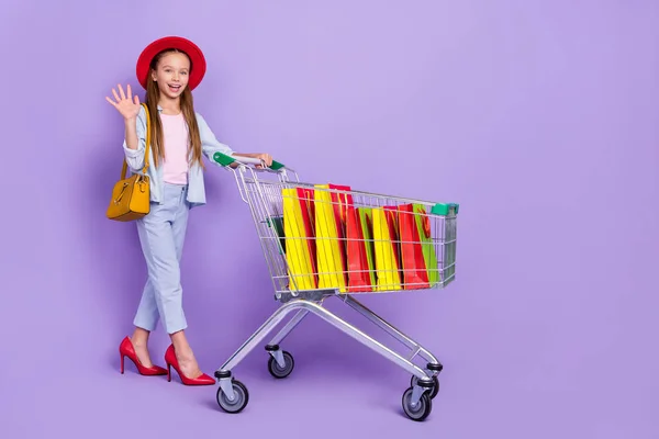 Photo of friendly small schoolgirl dressed jeans shirt red mom shoes handbag shopping tray isolated violet color background — Stock Photo, Image