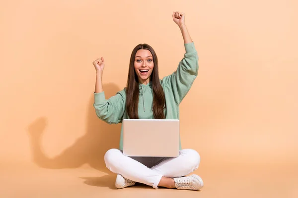Retrato de hermosa chica alegre de moda sentada usando el ordenador portátil regocijo éxito aislado sobre fondo de color pastel beige —  Fotos de Stock