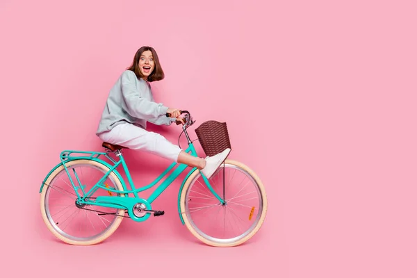 フルボディプロフィール写真の若い陽気な女性は、ピンクの色の背景に隔離された楽しい遊び心のある趣味のライドバイクを持っています — ストック写真