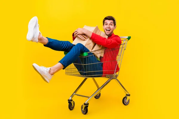 Full length body size view of attractive cheery guy sitting inside cart carrying buyings isolated on bright yellow color background — ストック写真