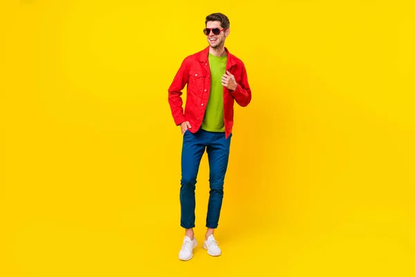 Full length photo of funky brunet millennial guy look empty space wear glasses shirt pants sneakers isolated on yellow background — стоковое фото