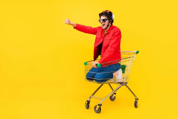 Volle Länge Körpergröße Ansicht der attraktiven fröhlichen Kerl im Wagen Spaß Reiten Narren isoliert auf leuchtend gelben Farbhintergrund — Stockfoto