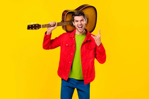 Portrét atraktivní veselý chlap drží kytaru ukazující klakson znamení baví izolované přes jasně žluté barvy pozadí — Stock fotografie