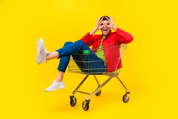 Volledige lichaamsomvang uitzicht van aantrekkelijke vrolijke man zitten in winkelwagen tonen ok-teken geïsoleerd op felgele kleur achtergrond — Stockfoto
