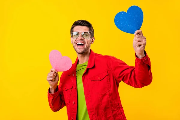 Foto de chico moreno joven lindo sostiene corazones usan gafas de camisa roja aisladas en el fondo de color amarillo —  Fotos de Stock