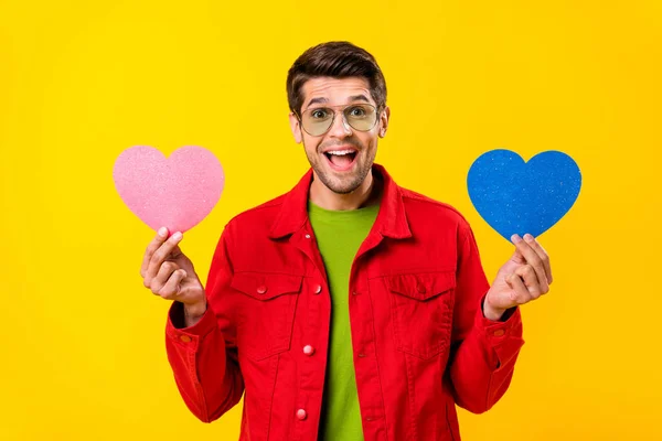 Photo of impressed millennial brunet guy hold hearts wear red shirt eyewear isolated on yellow color background — 스톡 사진