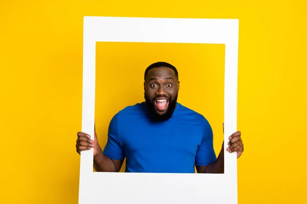 Portrét pohledný trendy ohromený veselý chlap drží foto rám dobrá nálada izolované přes jasně žluté barvy pozadí — Stock fotografie