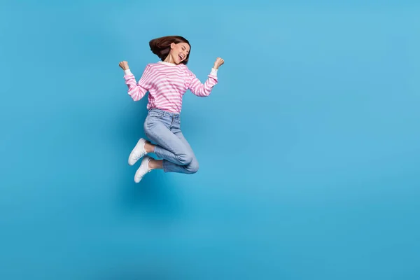 Foto di eccitata donna fortunata indossare maglione a righe alzando pugni saltando alto spazio vuoto isolato sfondo di colore blu — Foto Stock
