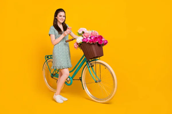 Foto von süßen entzückenden Frau tragen Print-Kleid Fahrrad fahren Chat moderne Gadget leeren Raum isoliert gelbe Farbe Hintergrund — Stockfoto