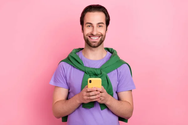 Foto van grappige duizendjarige baard man houden telefoon dragen paarse t-shirt groene sweater geïsoleerd op roze kleur achtergrond — Stockfoto