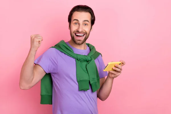 Foto di celebrare giovane barba uomo giocare telefono urlare indossare viola t-shirt verde felpa isolato su sfondo di colore rosa — Foto Stock