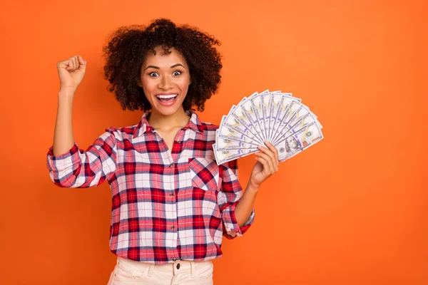 Photo of lucky funny young woman wear plaid shirt rising fist money fan empty space isolated orange color background — ストック写真