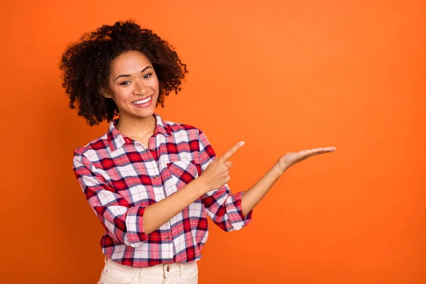 Photo of millennial curly lady hold index empty space wear plaid shirt isolated on orange color background — Stock Photo, Image