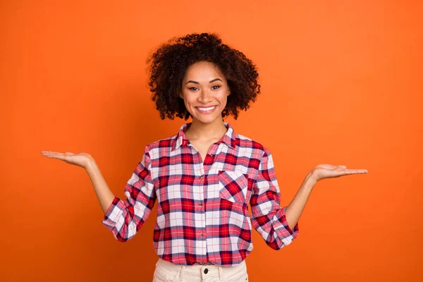 Photo of young curly lady hold empty space wear plaid shirt isolated on orange color background — ストック写真