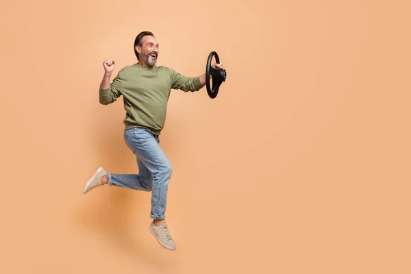 Full length profile photo of excited cheerful man look empty space vehicle wheel isolated on beige color background — Stock Photo, Image