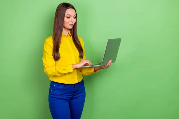 聪明的千年型棕色发式女士的照片看上去像笔记本电脑，穿的衬衫裤子与绿色背景隔离 — 图库照片