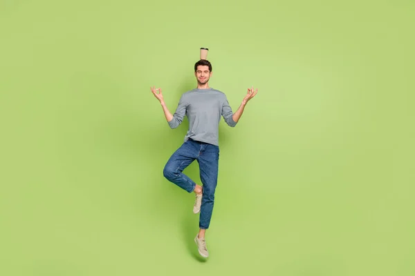 Foto de corpo inteiro de cara atraente fazendo ioga com xícara de chocolate quente na cabeça isolada no fundo de cor verde — Fotografia de Stock