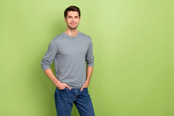 Фото милого молодого брюнет парень носить серый пуловер джинсы изолированы на зеленом фоне — стоковое фото