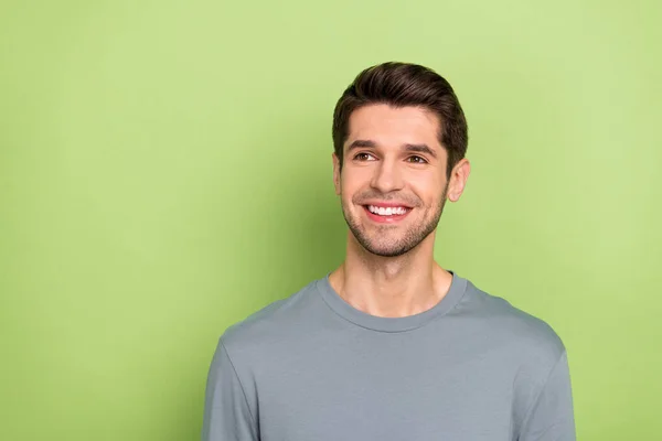 Photo of funny millennial brunet guy look empty space wear grey cloth isolated on green color background — 스톡 사진