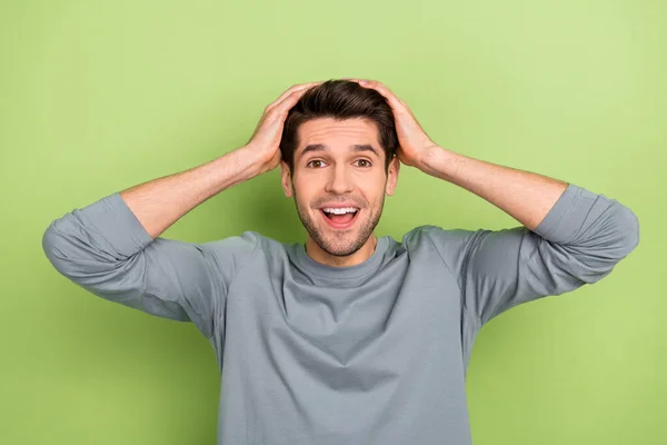 Fotografie ohromen tisíciletý brunet chlap ruce hlava nosit šedý svetr izolované na zeleném pozadí — Stock fotografie