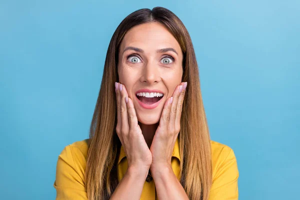 Foto di impressionato giovane acconciatura marrone signora mani viso usura camicia gialla isolato su sfondo di colore blu — Foto Stock