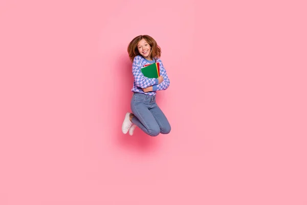 Full size foto di bionda piccola ragazza salto tenere libro usura maglione jeans scarpe da ginnastica isolato su sfondo rosa — Foto Stock