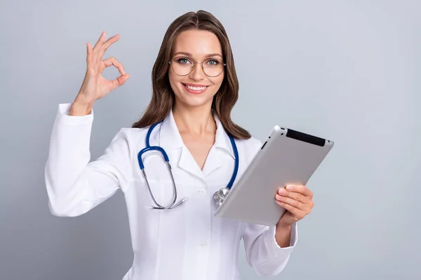Фотографія молодої жінки кардіолог використовує сучасний пристрій показують пальці символ джакузі рекомендують ізолювати на сіро-кольоровому фоні — стокове фото