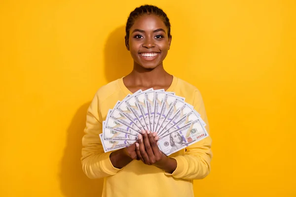 Portrait of attractive cheerful brunette girl holding in hands us atm cash isolated over bright yellow color background — ストック写真