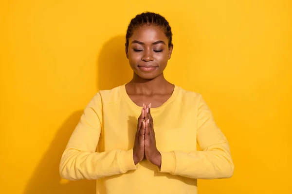 Портрет привабливої мрійливої дівчини, яка просить молитися складеними руками ізольовано на яскраво-жовтому тлі — стокове фото