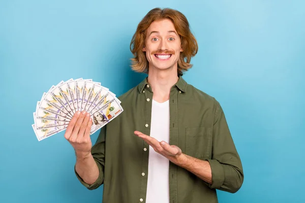 Portrait of attractive funky cheerful guy demonstrating us dollar 100 atm salary isolated over pastel blue color background — Stockfoto
