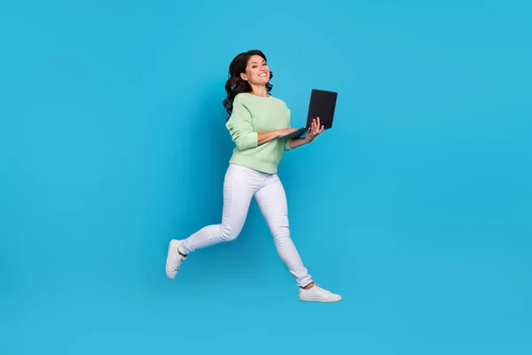 Full body photo of nice young brunette lady jump write laptop wear shirt pants sneakers isolated on blue background — Fotografia de Stock