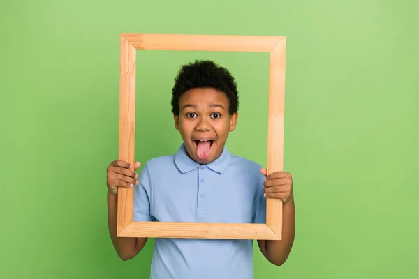 Portrait of handsome cheerful funny foolish pre-teen boy holding photo frame grimacing isolated over green color background — стоковое фото