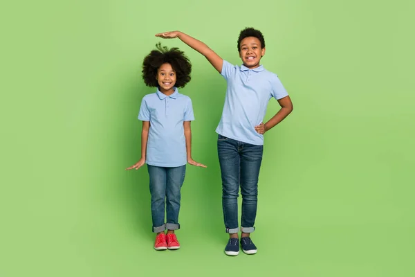 Full length body size view of two attractive trendy cheerful pre-teen kids measuring growth isolated over green color background — Stock Photo, Image