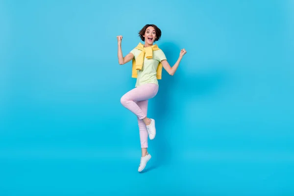 Full size photo of celebrate millennial brunette lady jump yell wear t-shirt pants shoes isolated on blue background — Stock Photo, Image