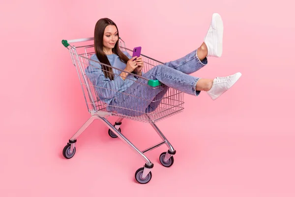 Full length body size view of attractive funny girl sitting in cart using device isolated over pink pastel color background — Photo