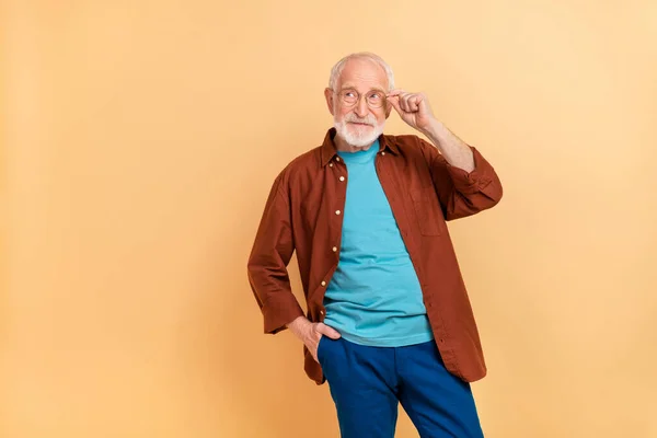 Foto av söt drömsk kille pensionär klädd brun skjorta armglasögon ser tomt utrymme isolerad beige färg bakgrund — Stockfoto
