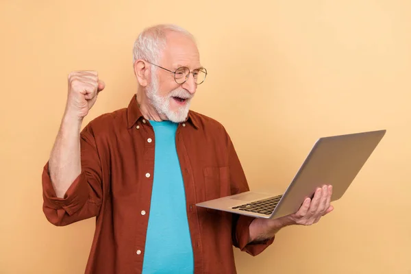 Photo of surprised lucky guy pensioner dressed brown shirt rising typing modern device isolated beige color background — Fotografia de Stock