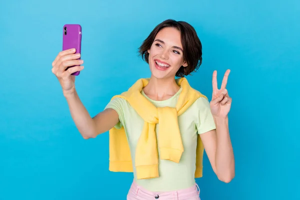 Photo of pretty funny woman wear green t-shirt recording video modern device showing v-sign isolated blue color background — стоковое фото