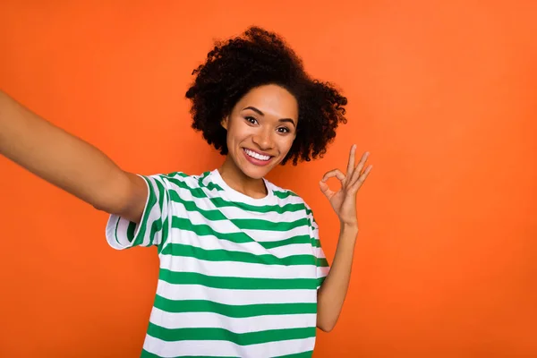 Autorretrato de atractiva chica de pelo ondulado alegre mostrando anuncio de anuncio ok-signo aislado sobre brillo fondo de color naranja — Foto de Stock